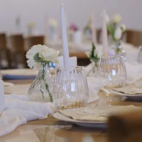 Elegant banquet table set for a formal event with tall white candles, crystal glassware, and white floral centerpieces in glass vases